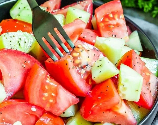 Fresh cucumber tomato salad garnished with herbs and served on a plate