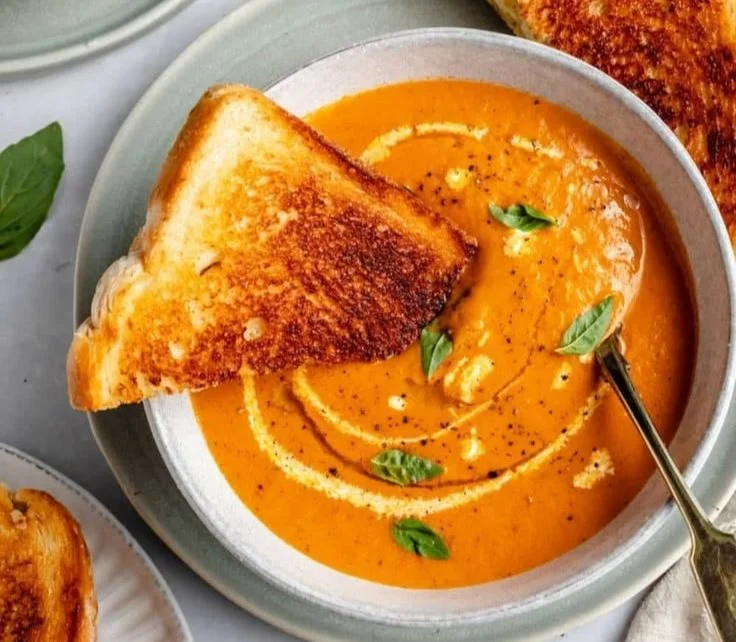 A bowl of delicious roasted tomato soup garnished with fresh basil and served with bread.