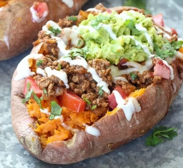 Taco stuffed sweet potatoes topped with avocado and salsa.